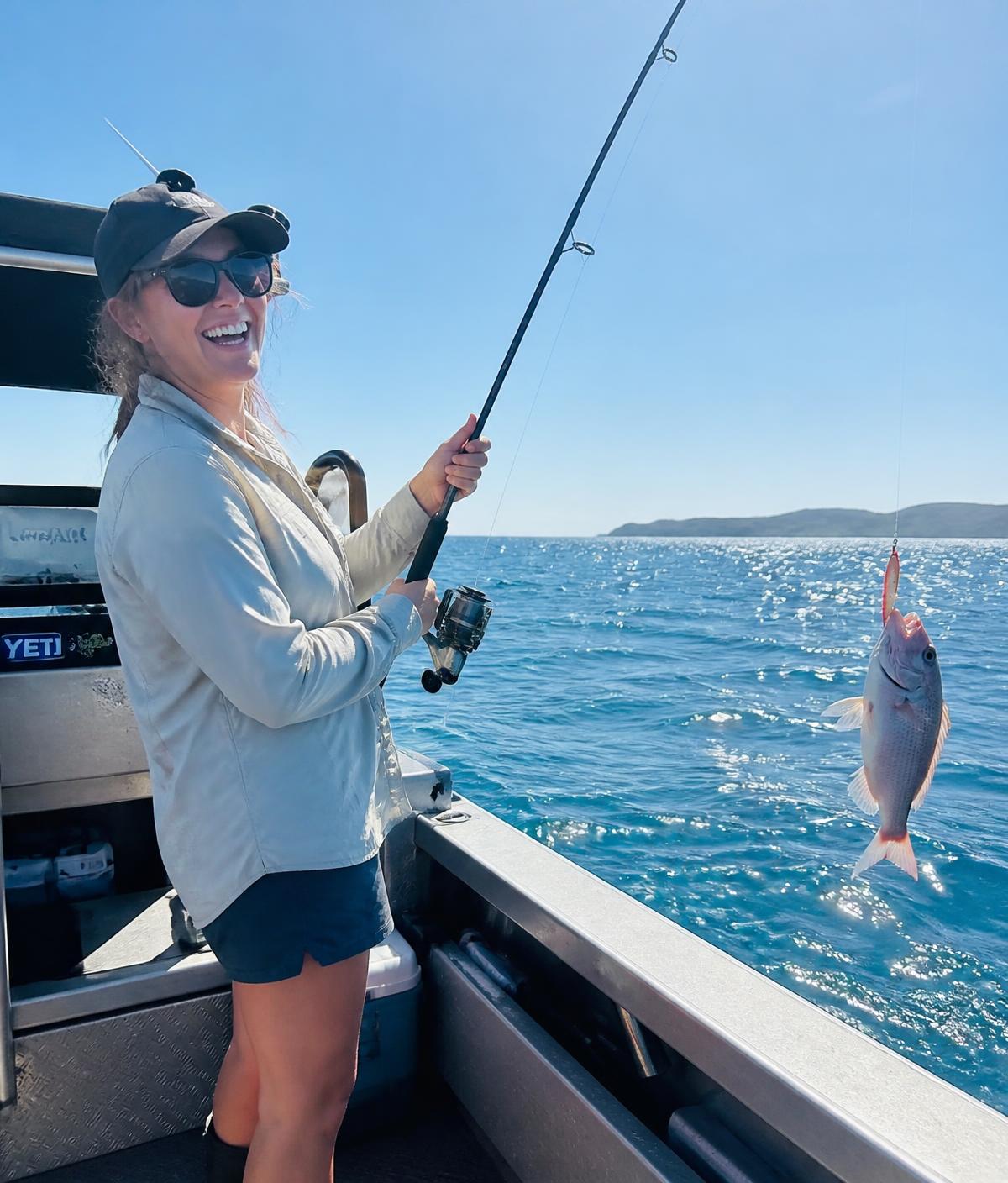 Angler on the deck of an aluminium boat landing a fish on a bright day in Australian bay waters