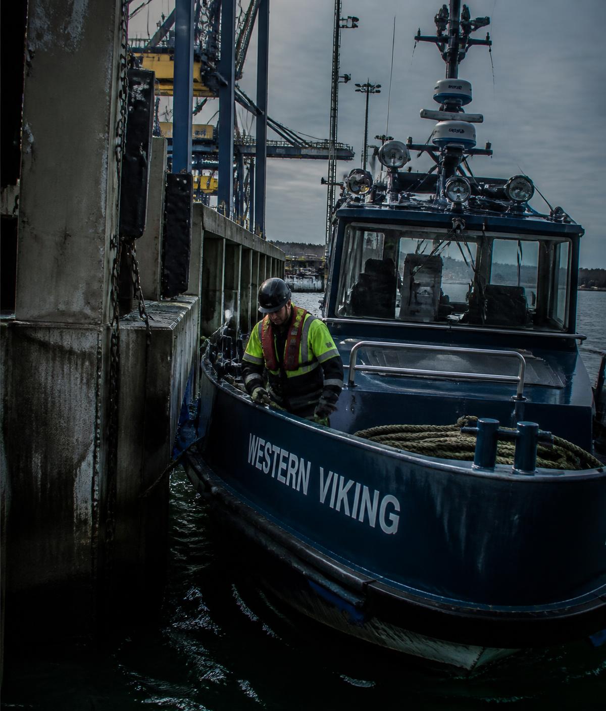 Deckhand in hi-vis working a commercial workboat alongside a concrete wharf under overcast light