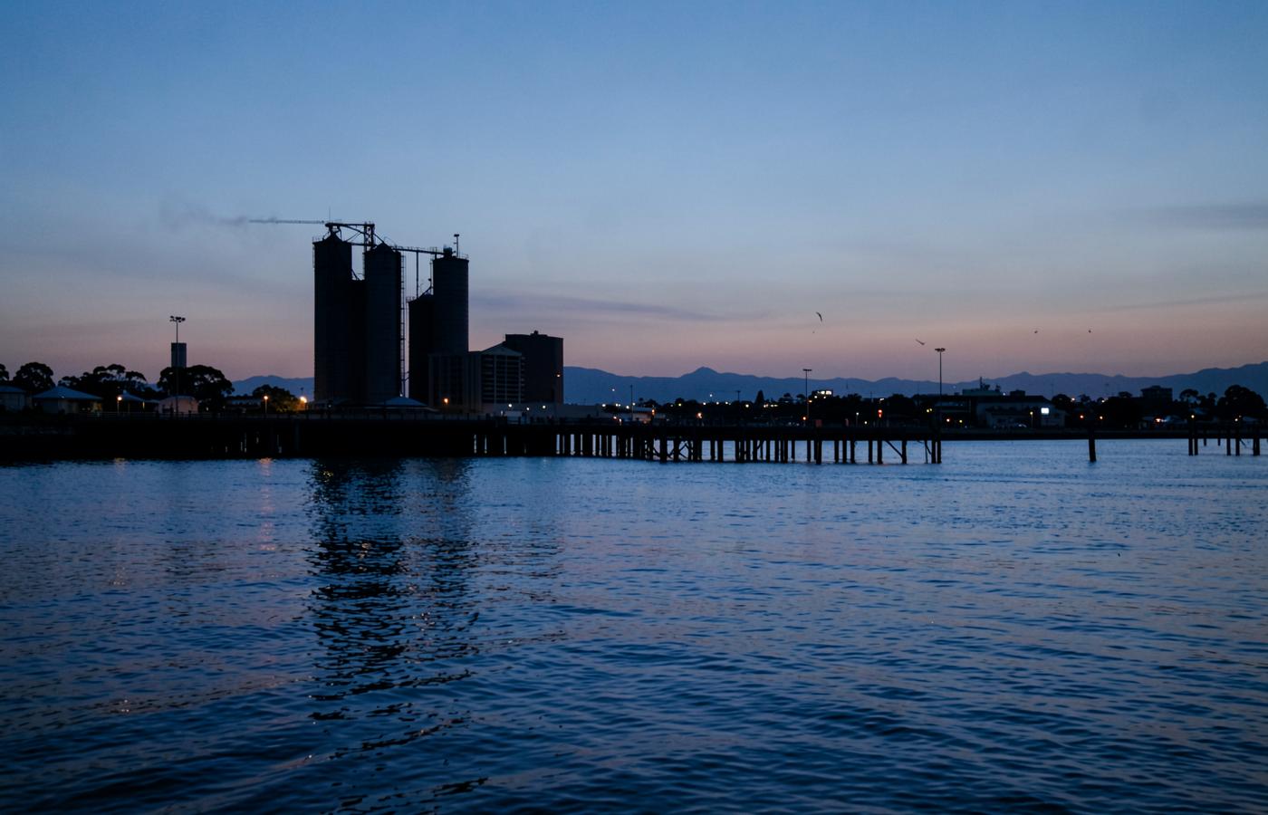 Geelong waterfront silos and pier silhouetted at dusk seen from the water