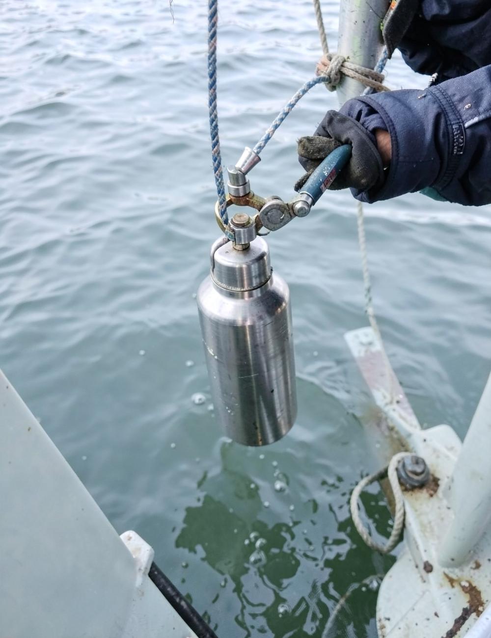 Stainless water sampling bottle being lowered from a workboat into bay water for environmental sample collection